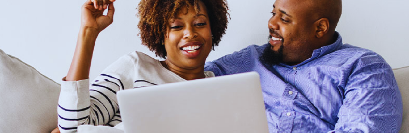 A man and a woman sitting on a couch together while looking at a laptop.